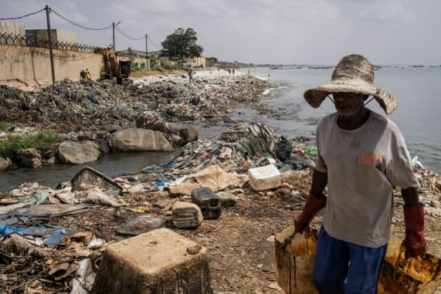 Um homem carrega baldes depois de despejar resíduos em um canal ao longo da Baía de Hann 