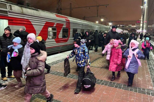 Crianças embarcando em um trem.  Eles estão vestindo jaquetas coloridas e carregando sacolas.