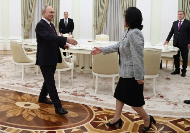 Vladimir Putin estende a mão enquanto caminha em direção ao ministro das Relações Exteriores da Coreia do Norte, Choe Son Hui, no Kremlin.  Ele está sorrindo e parece relaxado.  Ela também está estendendo a mão.