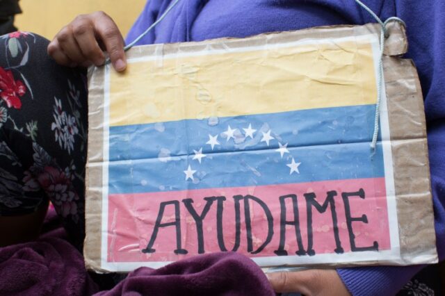 Um migrante venezuelano, cujo rosto não é visível na fotografia, segura uma placa que mostra a bandeira venezuelana com a frase, 