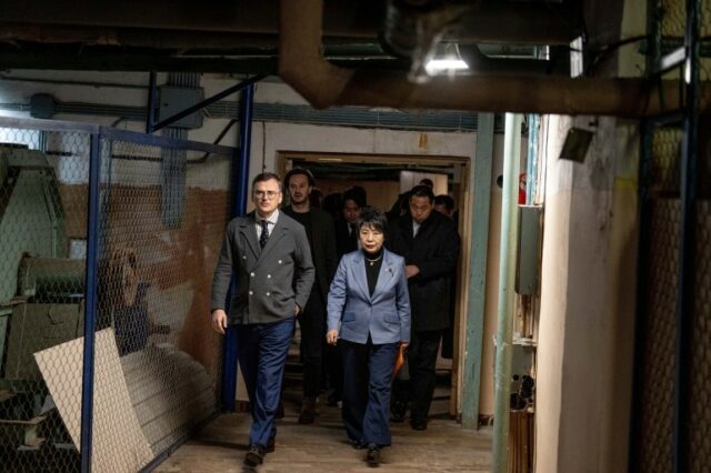 O ministro das Relações Exteriores da Ucrânia, Dmytro Kuleba, guia a ministra das Relações Exteriores do Japão, Yoko Kamikawa, por um corredor subterrâneo.  Existem grandes canos acima deles.