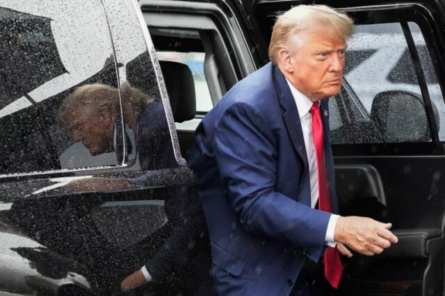 Donald Trump sai de um veículo SUV preto, vestindo terno azul e gravata vermelha.