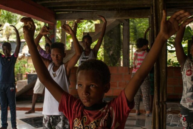 Um grupo de crianças levanta os dois braços enquanto pratica salsa em Buenaventura, Colômbia.
