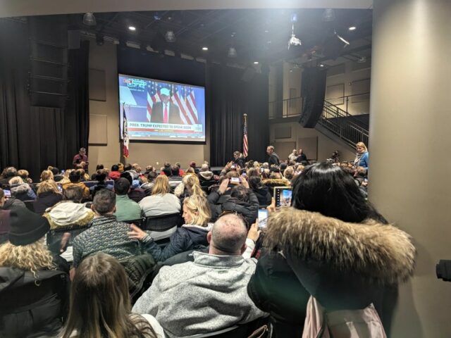 Apoiadores de Trump em uma sala lotada assistem o ex-presidente falando em uma tela