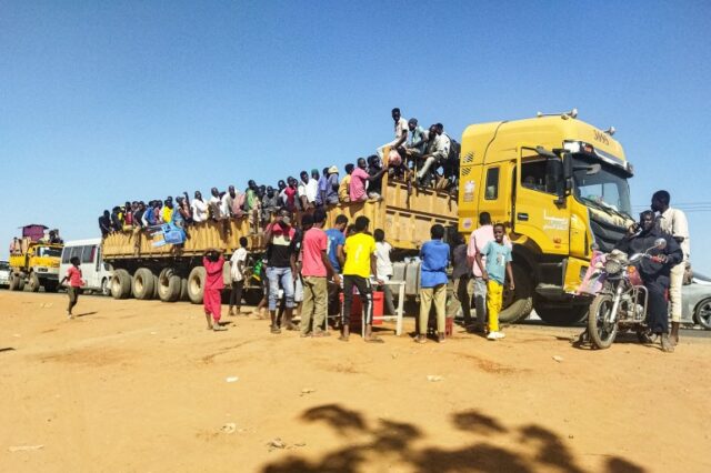 Pessoas deslocadas pelo conflito no Sudão sobem na traseira de um caminhão que circula por uma estrada em Wad Madani, capital do estado de al-Jazirah, em 16 de dezembro de 2023. (Foto AFP)