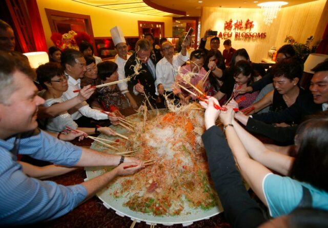 Os convidados jogam um prato de 88 kg de yusheng ou peixe cru durante um 