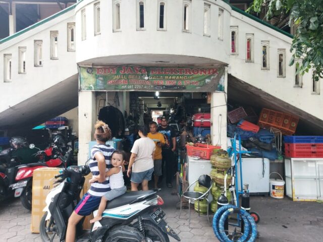 O exterior do Mercado Notoharjo.  Há uma balaustrada subindo.  Há pessoas do lado de fora, incluindo uma mulher em uma motocicleta com uma criança nas costas