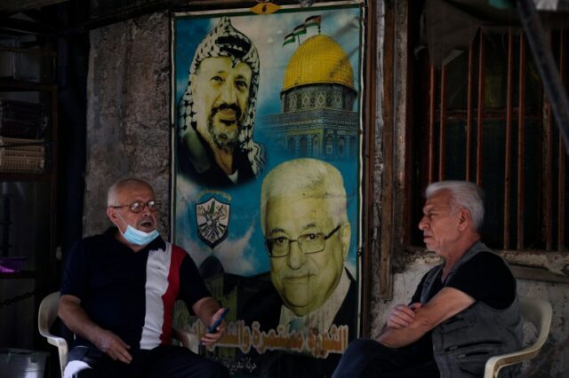 Palestinos falam sentados ao lado de um pôster do falecido líder palestino Yasser Arafat, à esquerda, e do presidente palestino Mahmoud Abbas, à direita, no campo de refugiados palestinos de Bourj al-Barajneh, em Beirute, Líbano, sexta-feira, 21 de outubro de 2022. O colapso económico histórico do Líbano está a afectar duramente os refugiados palestinianos na pequena nação onde a grande maioria deles vive agora na pobreza, enquanto outros arriscam as suas vidas em busca de um futuro melhor no estrangeiro, disse sexta-feira a agência da ONU para os refugiados palestinianos.  (Foto AP/Bilal Hussein)