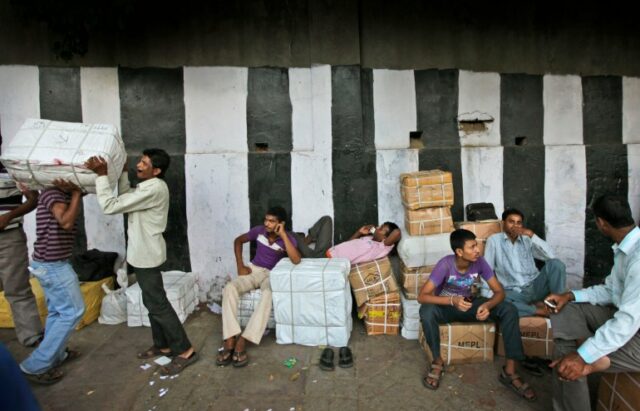Trabalhadores indianos descansam perto de mercadorias antes de transportá-las em Nova Delhi, Índia