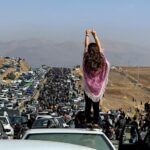 Uma mulher sem véu em cima de um veículo enquanto milhares de pessoas se dirigem ao cemitério de Aichi em Saqez, a casa de Mahsa Amini