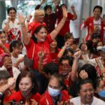 Apoiadores de Pheu Thai.  Eles estão vestidos de vermelho, sorrindo e torcendo.