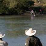 Uma família de migrantes cruza o rio Rio Grande logo atrás da entrevista coletiva de um legislador republicano criticando as políticas de imigração do governo Biden durante uma visita a Eagle Pas
