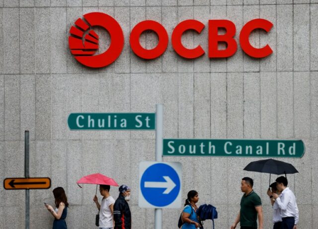 Exterior do Banco OCBC em Singapura com pessoas passando.  Eles estão segurando guarda-chuvas.