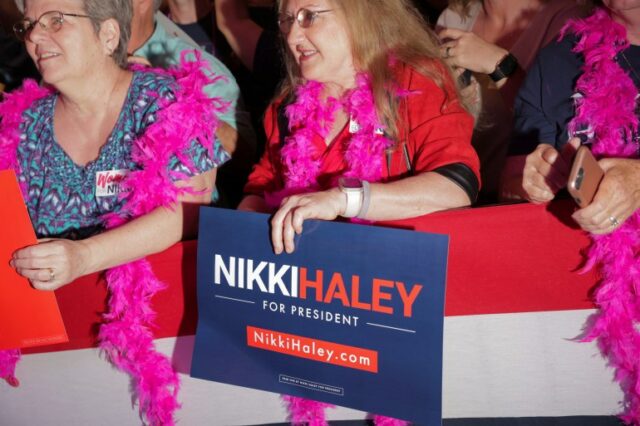 Um apoiador de Nikki Haley usa um boá de penas e segura uma placa em apoio ao candidato.