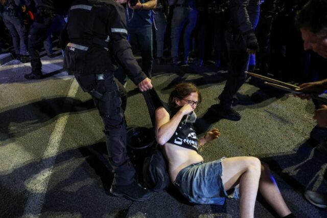 Um oficial segura as roupas de um manifestante enquanto manifestantes antigovernamentais iniciam uma manifestação prolongada 