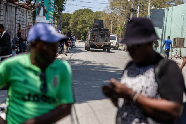 Um tanque blindado da polícia passa por pessoas em Porto Príncipe