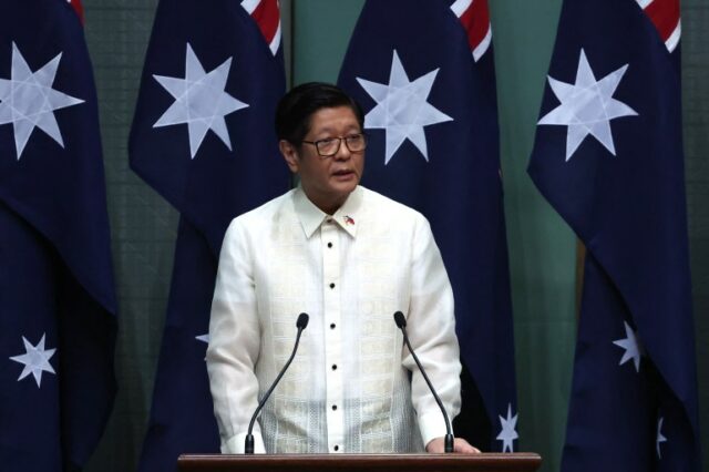 um homem de camisa branca fala em frente às bandeiras australianas