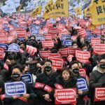 Uma multidão de médicos nas ruas de Seul.  Eles carregam cartazes mostrando sua oposição aos planos de aumentar o número de vagas nas escolas médicas