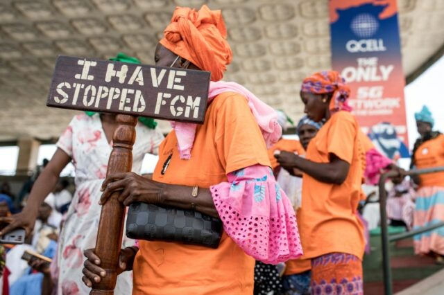 Uma manifestante anti-mutilação genital feminina (MGF) segura um cartaz em frente à Assembleia Nacional em Banjul, em 18 de março de 2024, durante o debate entre legisladores sobre um projeto de lei altamente polêmico que busca suspender a proibição da MGF