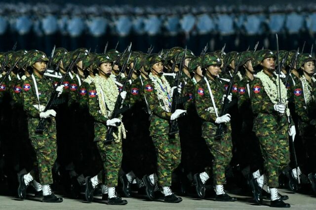 Mulheres soldados de Mianmar marcham em seu desfile.  Eles estão carregando armas e alguns têm várias guirlandas de flores em volta do pescoço