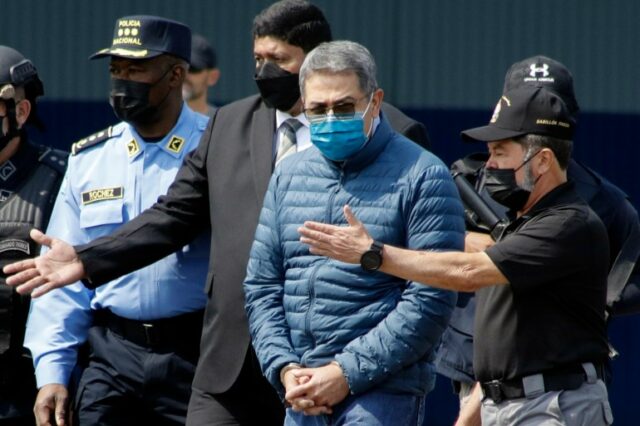 Juan Orlando Hernandez, com máscara facial e jaqueta azul, é escoltado por policiais.