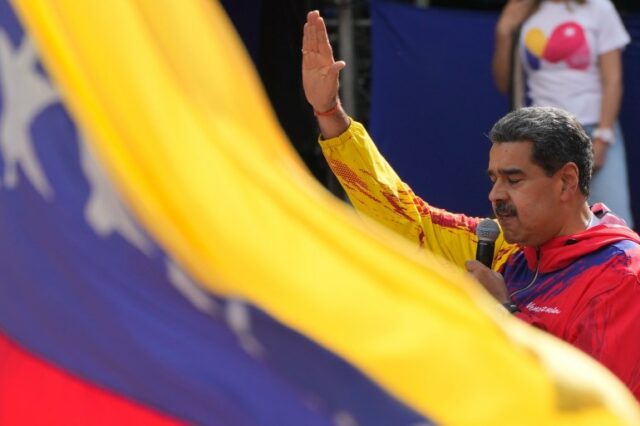 Nicolas Maduro acena atrás de uma bandeira venezuelana.