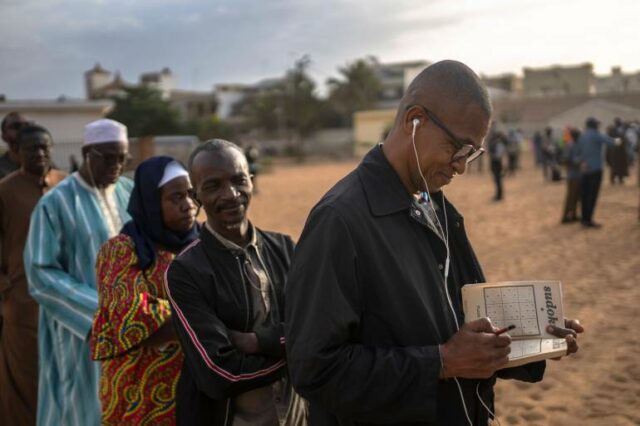 Um homem resolve um enigma sudoko enquanto espera na fila para votar fora de uma seção eleitoral durante as eleições presidenciais, em Dakar, Senegal, domingo, 24 de março de 2024. (AP Photo/Mosa'ab Elshamy)