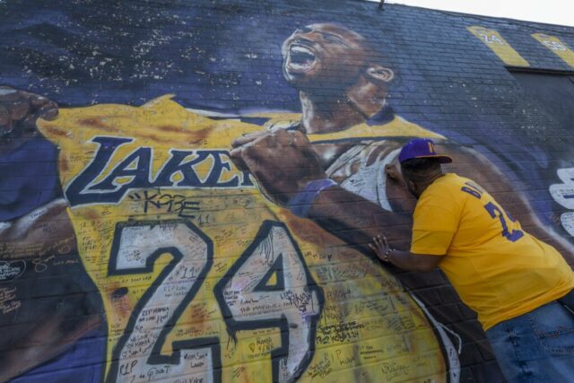 Um fã escreve uma mensagem em um mural para o ex-astro do basquete do Los Angeles Lakers, Kobe Bryant, durante a cerimônia oficial em memória dele e de sua filha, Gianna, no vizinho Staple Center, em 24 de fevereiro de 2020, em Los Angeles, Califórnia.  Kobe e sua filha de 13 anos, que estavam entre as nove pessoas mortas em um acidente de helicóptero em 26 de janeiro, enquanto voavam para sua Mamba Sports Academy, onde ele a treinaria em um torneio.