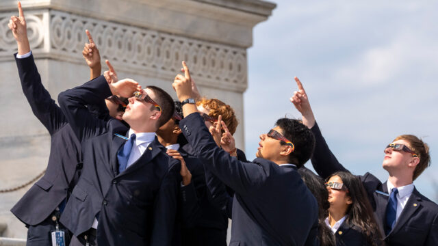 As páginas do Senado usam óculos para eclipse enquanto veem a lua cobrindo parcialmente o sol durante um eclipse solar total no Capitólio, segunda-feira, 8 de abril de 2024, em Washington.