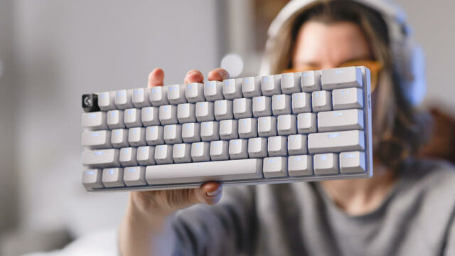 Uma mulher com um suéter cinza segura um teclado para jogos Logitech G Pro X 60 branco até a câmera com a mão esquerda.