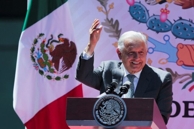 Andres Manuel Lopez Obrador acena atrás de um pódio, ao lado de uma bandeira mexicana.