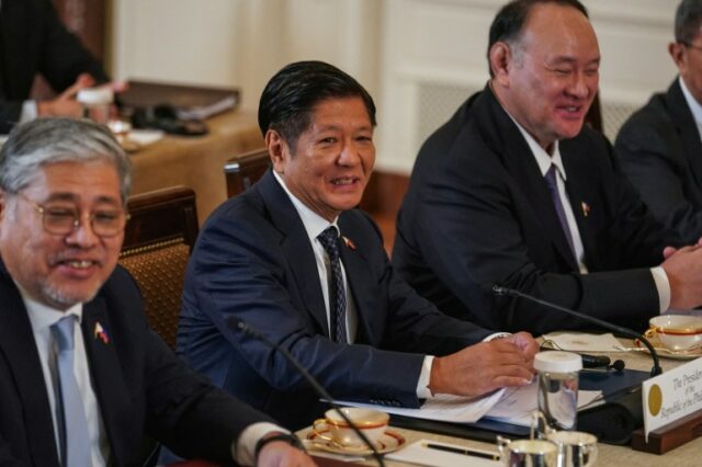 O presidente filipino, Ferdinand Marcos Jr, participa de uma cúpula trilateral com o presidente dos EUA, Joe Biden, e o primeiro-ministro do Japão, Fumio Kishida.  Ele está sentado a uma mesa entre dois de seus oficiais.  Eles estão sorrindo.