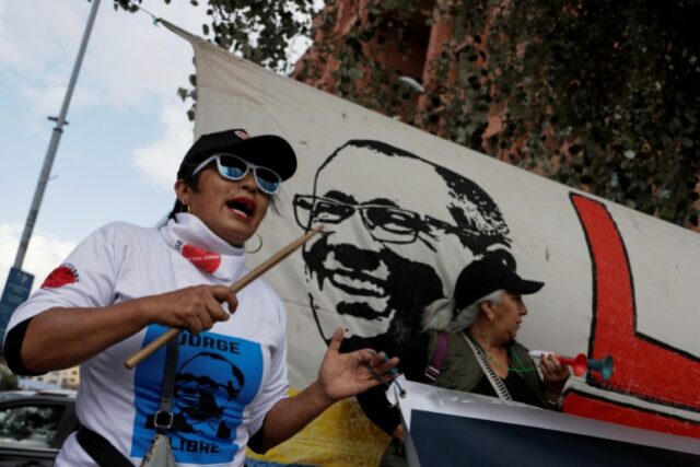 Uma mulher canta enquanto se manifesta diante de uma faixa com o rosto de Jorge Glas.