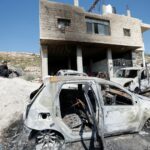 Um homem palestino sentado perto de uma casa e carros danificados depois que colonos israelenses atacaram a vila de al-Mughayyer, na Cisjordânia ocupada por Israel, 13 de abril de 2024