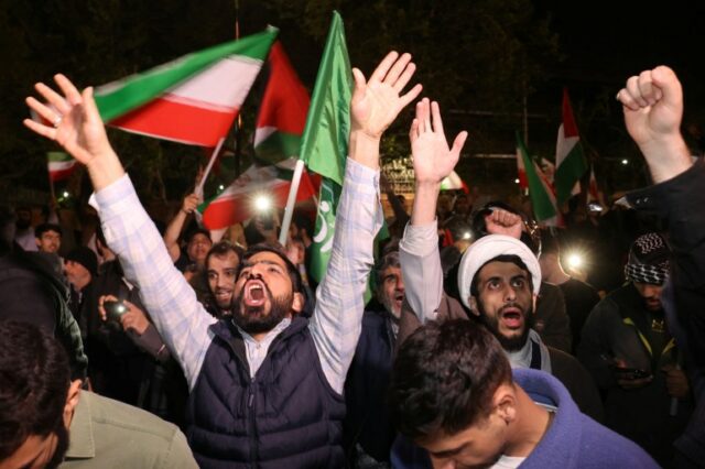 homens levantam os braços em um protesto à noite com bandeiras palestinas