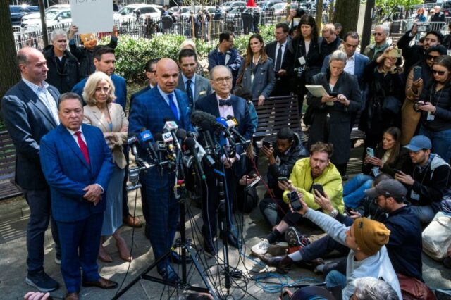 O advogado de Harvey Weinstein, Arthur Aidala, falando à mídia após a decisão do tribunal de Nova York, Ele está vestindo um terno azul e é careca.  Ele está diante de um conjunto de microfones.  Outros estão ao lado dele.  Alguns dos jornalistas estão agachados na frente.