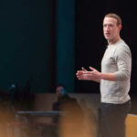 Mark Zuckerberg no palco durante uma apresentação da empresa.  Vista de perfil do lado esquerdo.