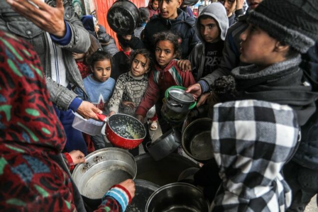 Palestinos segurando tigelas vazias recebem alimentos distribuídos por voluntários de instituições de caridade como pessoas que enfrentam crise de fome e risco de fome devido ao embargo israelense imposto ao território, em Rafah, Gaza, em 18 de fevereiro