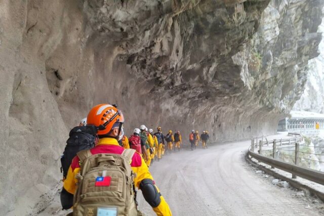 Equipes de resgate caminhando sob um enorme afloramento rochoso ao longo de uma estrada