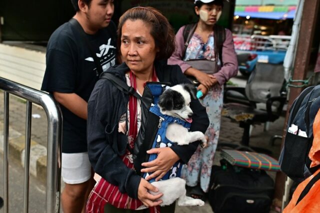 Uma mulher de Myawaddy carregando seu cachorro enquanto espera para cruzar para a Tailândia.  O cachorro é preto e branco e usa um arnês azul