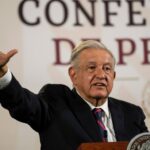 Andres Manuel Lopez Obrador fala em um pódio, levantando uma mão estendida em gesto.