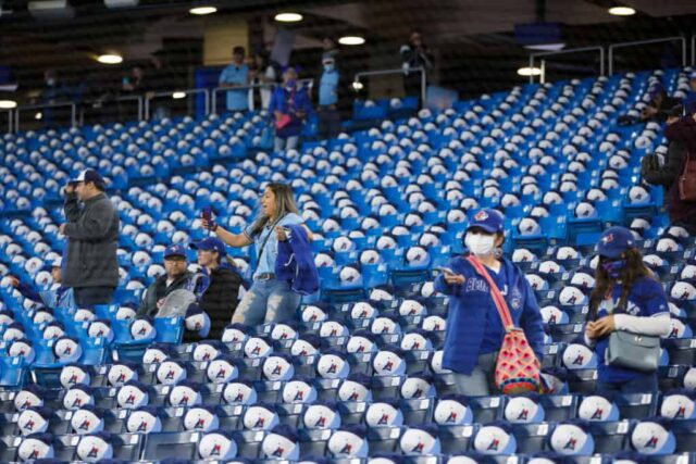 Os fãs se aglomeram enquanto os chapéus sentam nos assentos durante o treino de rebatidas antes do jogo da MLB entre o Toronto Blue Jays e o Texas Rangers no dia de abertura no Rogers Centre em 8 de abril de 2022 em Toronto, Canadá.