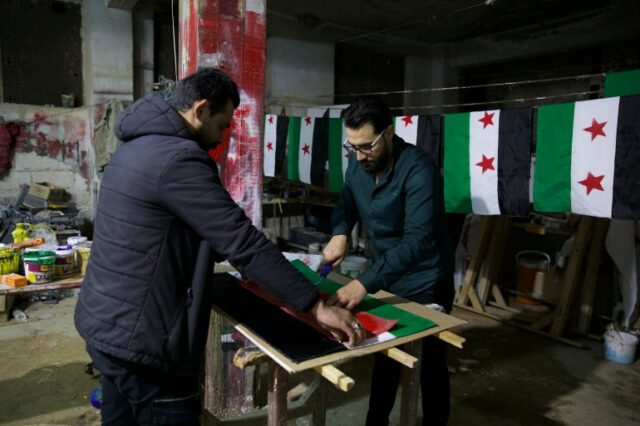 Dois homens preparam uma bandeira da oposição síria