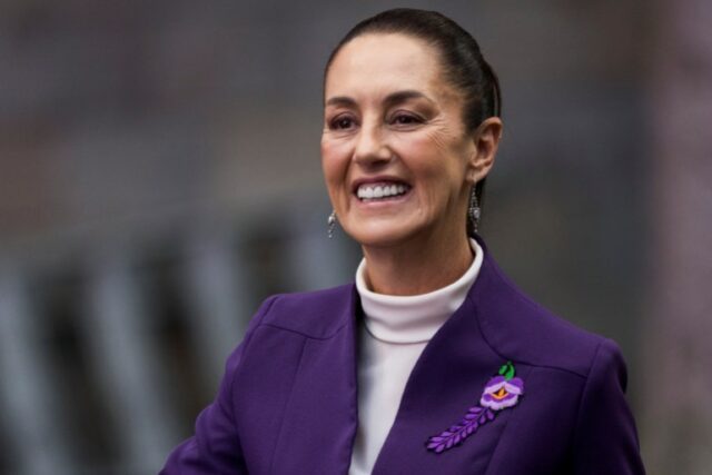 Claudia Sheinbaum está sorrindo, vestindo um blazer roxo.