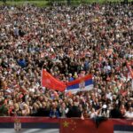 Pessoas agitando bandeiras chinesas e sérvias se reúnem em frente ao Palácio da Sérvia durante uma cerimônia de boas-vindas ao presidente chinês, Xi Jinping, em Belgrado.