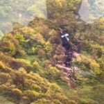 Uma área negra queimada na encosta de uma montanha arborizada.  A cauda azul e branca de um helicóptero pode ser vista.