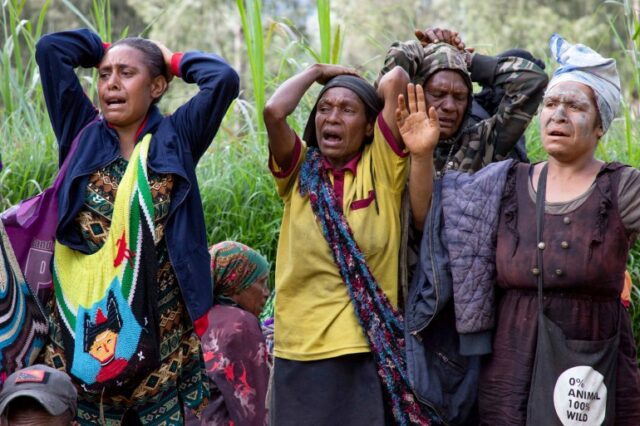 Mulheres perturbadas assistem aos esforços de resgate no local de um enorme deslizamento de terra em PNG.  Eles colocam as mãos na cabeça.  Uma delas fechou os olhos.