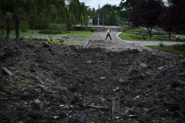 Uma enorme cratera deixada por um míssil russo durante um ataque a Zaporizhzhia.  Uma mulher está andando atrás.