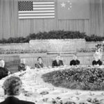 O presidente dos EUA, Richard, e a primeira-dama Pat Nixon em uma enorme mesa de banquete em sua visita à China em 1972. O primeiro-ministro chinês, Zhou Enlai, está do outro lado da mesa.  As bandeiras da China e dos EUA estão expostas na parede atrás delas