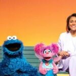 Muppets Elmo, Cookie Monster e Abbey sentam em um banco com a atriz Ariana DeBose